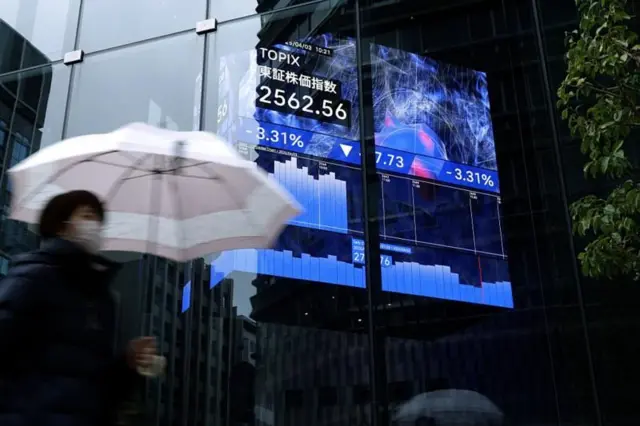 የንግድ ዋጋ ለውጥን በሚያሳይ ስክሪን በኩል ሻንጥላ የያዘች ሴት ስታልፍ