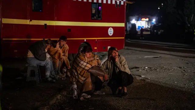 Загорнуті в ковдри люди сидять біля пожежної машини