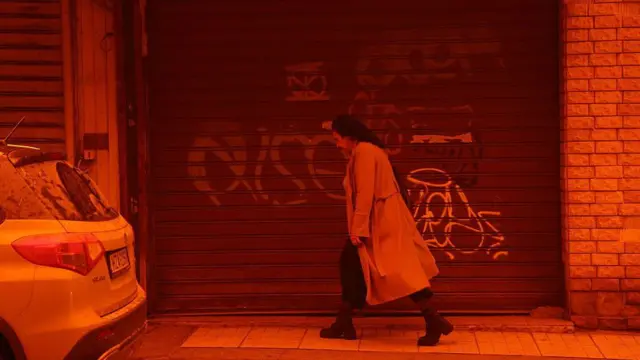 Крит покрыт облаком пыли из Сахары: человек идет вдоль домов, все вокруг красно-оранжевое