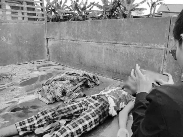 ထရပ်ကားအနောက်ပိုင်းမှာ ပက်လက်အနေအထားနဲ့ လဲနေတဲ့ ကလေးရုပ်အလောင်းနဲ့ အလောင်းကို ဓာတ်ပုံရိုက်နေသူတစ်ဦး