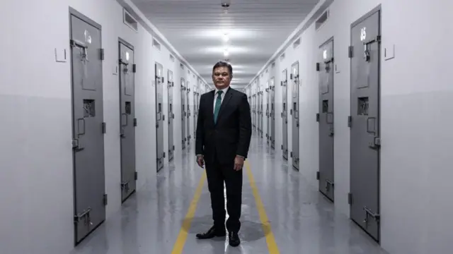 Lincoln Gakiya em um corredor penitenciário, com portas de ferro fechadas dos dois lados e ele no meio.  