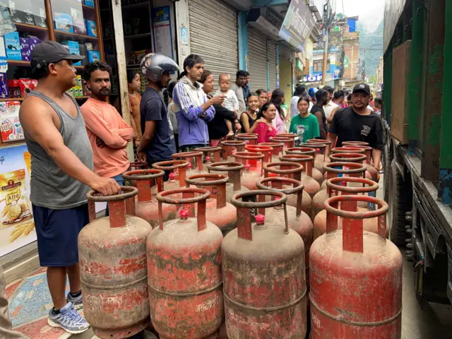 सिलिन्डर पर्खिरहेका मानिसहरू ग्यास भरिएका सिलिन्डरसँग