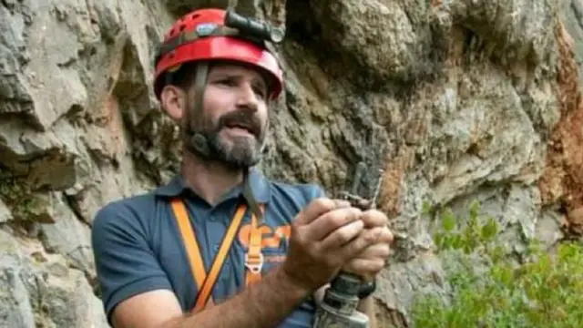 Homem branco de cabelo preto com equipamentos de exploração de caverna