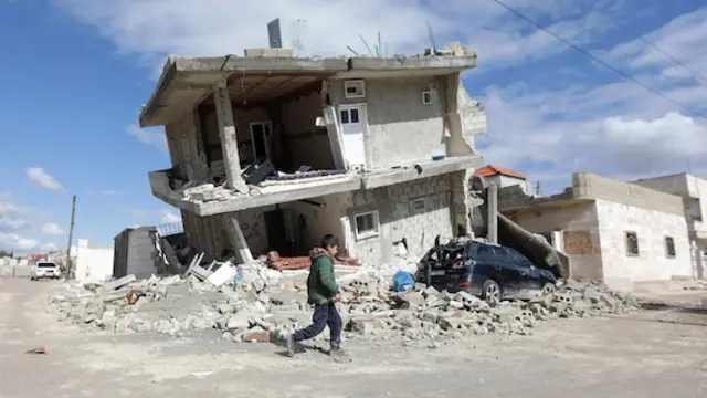 Un enfant marche devant une maison écroulée