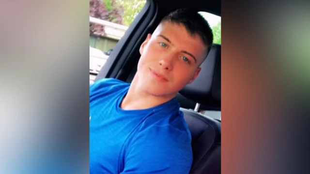 Lloyd Donkin está sentado en un coche, mirando a la cámara. Tiene el pelo corto y negro y lleva una camiseta azul.