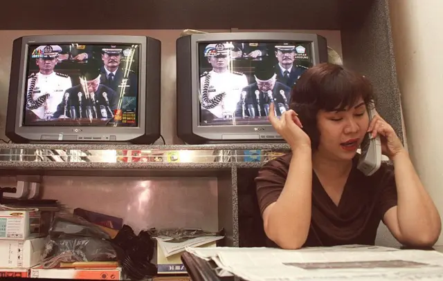Seorang wanita etnis Cina berbicara di telepon, di depan televisi yang menampilkan Presiden Indonesia kala itu, Soeharto.