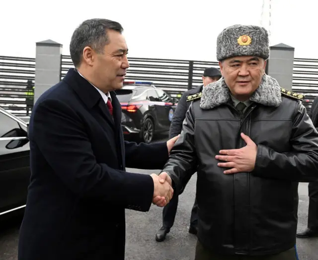 Садыр Жапаров (слева) жмет руку Камчыбеку Ташиеву на открытии здания Военно-медицинской службы ГКНБ, январь 2026 года
