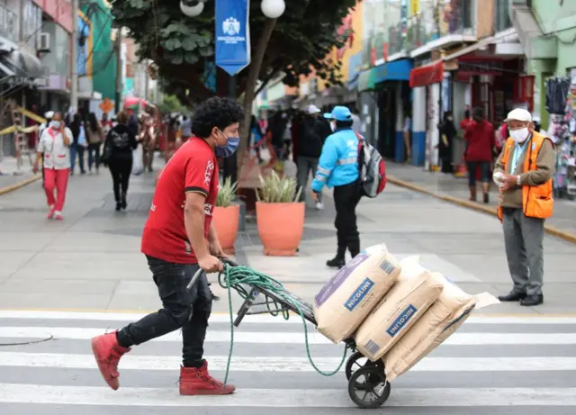 Un hombre empuja un carro cargado con sacos en una concurrida calle de Lima.