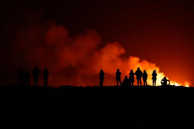Silueta de personas que observan el cielo y el humo rijizo luego de la erupción de un volcán en Islandia 