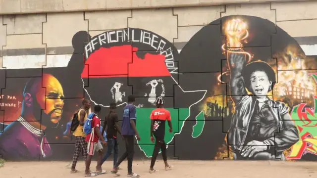 Un groupe de cinq garçons observent la fresque murale en passant devant le mur où elle se trouve. La fresque recouvre le mur.