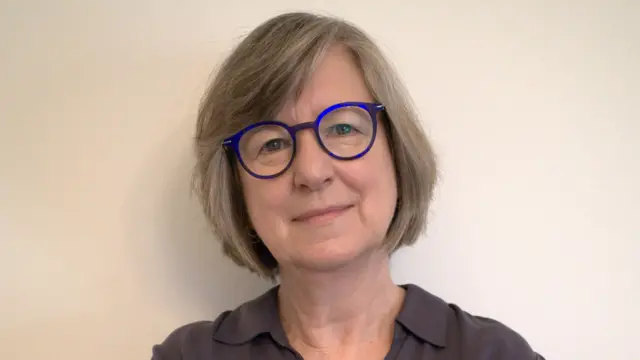 Maryellen MacDonald é uma mulher branca, de cabelos grisalhos e curtos. Ela está sorrindo para foto e usa óculos.