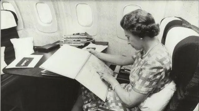 Fotografía de la reina Isabel II en el Concorde en 1977. La imagen es de British Airways y la monarca aparece trabajando en una mesa a bordo del avión.