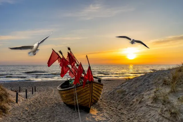 Atardecer en la playa de Usedom con gaviotas y un barco de pesca.