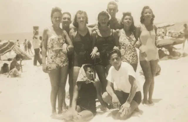Nove banhistas, seis mulheres e três homens, posam em praia movimentada no Rio de Janeiro, em foto antiga, em sépia, tirada em 1946. As mulheres estão todas usando maiô.