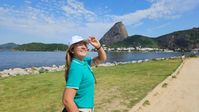 Mulher sorrindo em pé, de boné, em frente ao Pão de Açucar, no Rio