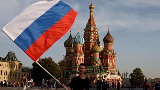 Jovem agita bandeira russa na frente da praça Vermelha, em Moscou