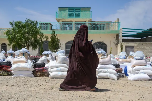 زنی در قندهار که برای دریافت کمک آمده از کنار خریطه های کمک‌های بشردوستانه می‌گذرد