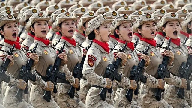 Soldadas de uniforme e boina marcham com fuzis