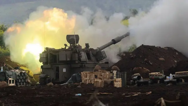 Bir tank ateş ediyor, etrafta dumanlar ve askeri malzeme var