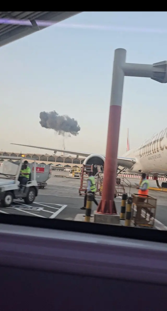 Unos trabajadores del aeropuerto de Dubái junto a un avión ven una columna de humo detrás de una de las terminales.