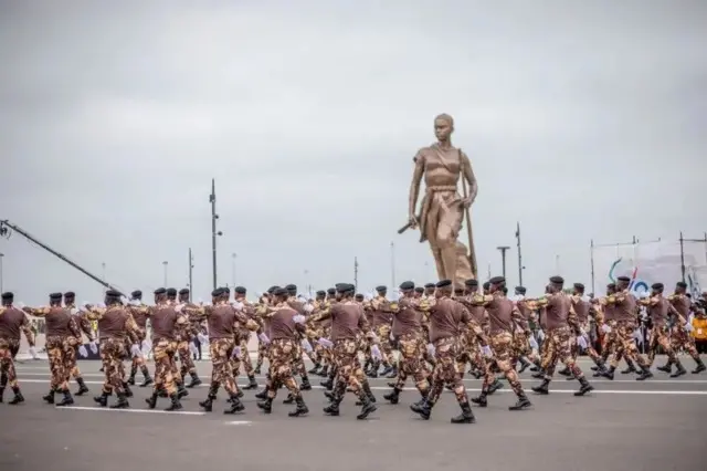 Des militaires béninois défilent devant la statue de l'Amazone à Cotonou.