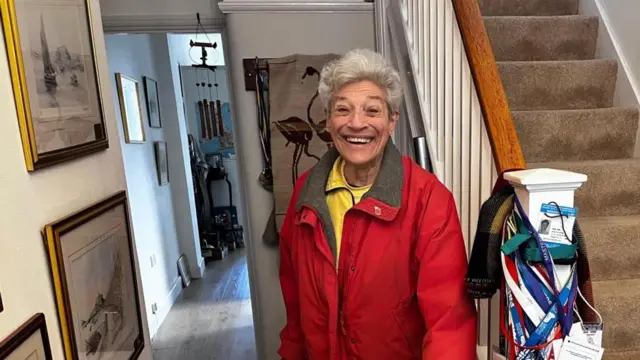 Jane Asher dentro de su casa, junto a una escalera en la que se ven medallas colgadas
