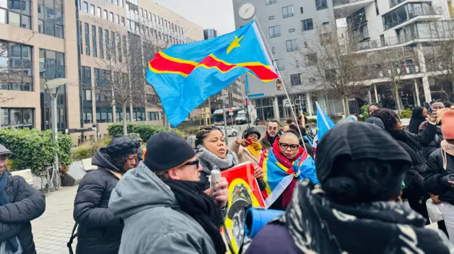 Abantu bahagaze hagati y'amagorofa y'inyubako ndende bafise n' amabendera