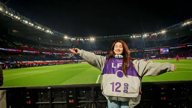 杜黝黝身穿记者服在球场边展开双臂，闭眼微笑