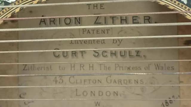 Vista del interior de la abertura del cuerpo del instrumento. En el interior se lee: La cítara Arion [PATENTE] Inventada por Curt Schulz, cítara de Su Alteza Real la Princesa de Gales, 43, Clifton Gardens, Londres, 1882