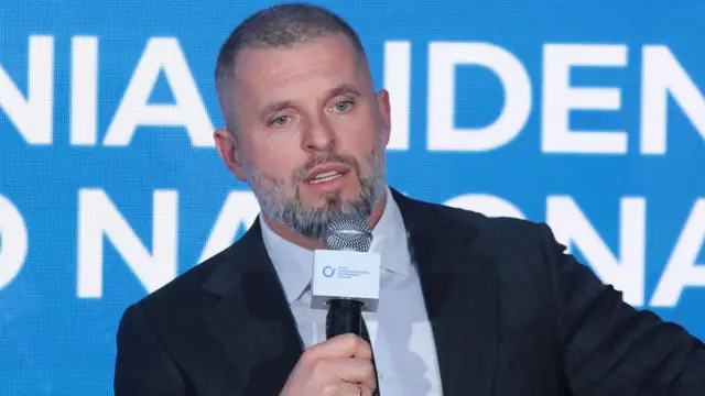 Матвей Бедный в темном костюме с микрофоном