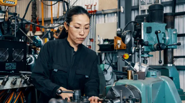 Egy nő gépi berendezést használ egy japán fémmegmunkáló üzemben