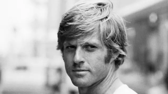 若いころのレッドフォードさんの白黒写真。かすかに微笑みつつ鋭い目つきでカメラの向こうを見ている