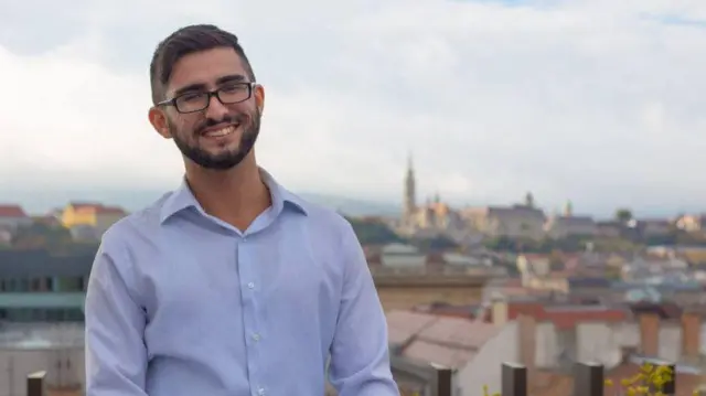 Bəhruz Səmədov gülümsəyir, arxa fonda Avropa şəhərlərindən biri