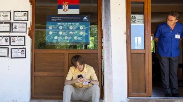 Dečak sedi, muškarac stoji pored njega ispred glasačkog mesta