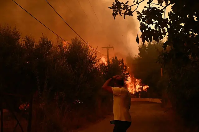 أحد السكان يسير في الطريق بينما تستعر حرائق الغابات قرب مدينة باتراس، غرب اليونان، في 13 أغسطس/آب 2025.