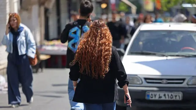 جوانان ایرانی در ۲۳ فروردین ۱۴۰۵ در خیابانی در تهران در حال عبور هستند. محمدباقر قالیباف، رئیس مجلس ایران که در مذاکرات صلح این آخر هفته با ایالات متحده حضور داشت، در همان روز اعلام کرد که واشنگتن در جریان این گفتوگوها “ناتوان” از جلب اعتماد تهران بوده است.