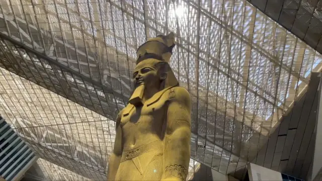 মিশরের ফারাও তুতেনখামুনের ভাস্কর্য, ওপরে জালের মতো কয়েকটি স্তরের ছাদ ভেদ করে সূর্য দেখা যাচ্ছে