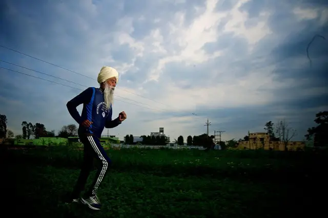 Fauja Singh koşu antremanı yapıyor. Eşofmanı, uzun sakalı ve türbanı ile dikkat çekiyor.