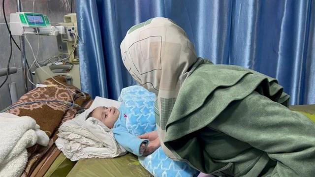 Mulher de costas segurando a mão de bebê em leito de hospital
