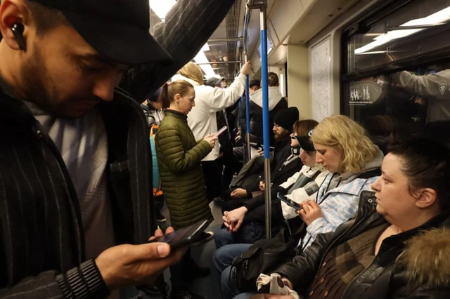 در یک قطار زیرزمینی، مسافران نشسته و ایستاده‌اند و برخی به گوشی موبایل خود نگاه می‌کنند