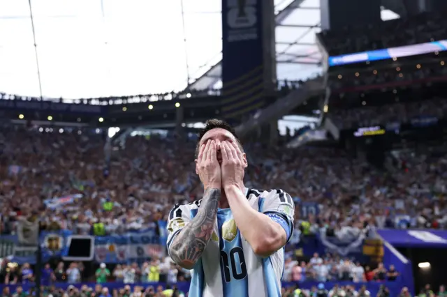 Messi con las manos sobre su rostro, y una tribuna del estadio repleta de aficionados detrás.