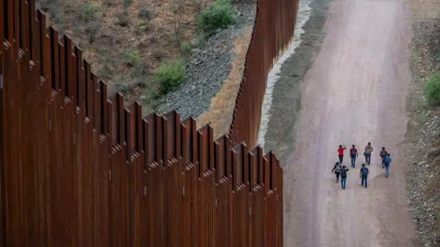 Migrantes procedentes de Centroamérica y Sudamérica, que buscan asilo, caminan junto a la valla fronteriza tras haber cruzado ilegalmente hacia Estados Unidos el 24 de junio de 2024 en Ruby, Arizona.