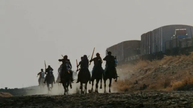 د شولې فلم یوه عکس کې سړي په سیلویټ انځورونو کې وسلې چلوي او په اسونو سپاره دي، او د دوړو سپین فلم شاته پریږدي.