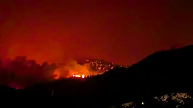山のシルエットの向こう側に、赤い炎と煙が上がっている。夜空が赤く染まっている