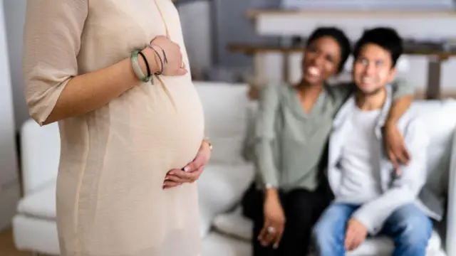 A couple looking at a surrogate mother who's touching her baby bump 