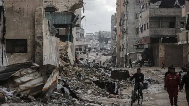 فلسطينيون يمرون أمام مبانٍ مدمرة خلال وقف إطلاق النار بين إسرائيل وحماس في حي الرمال في مدينة غزة