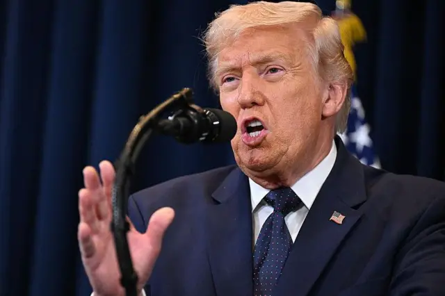 ټرمپ ولاړ دی لاس یې پورته کړی خبرې کوي.