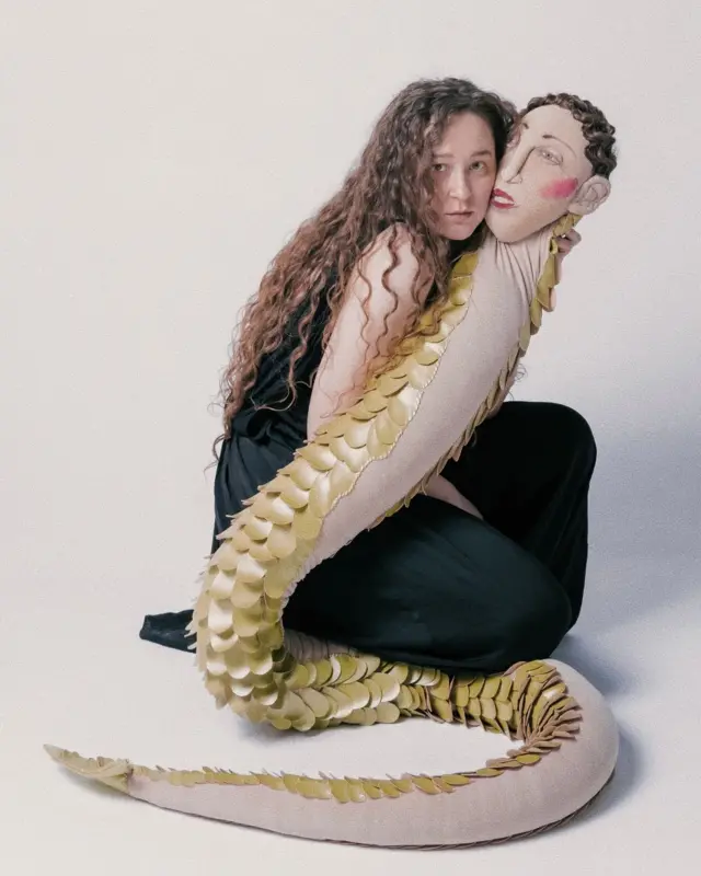 Женщина обнимает игрушку в виде мужчины-змеи