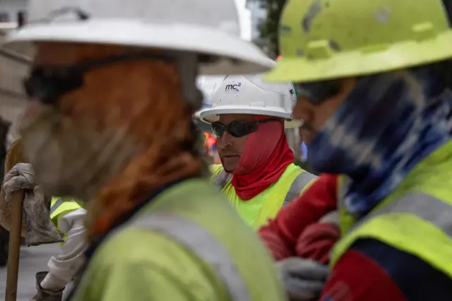 رجال يرتدون قطعة قماش مخصصة لتبريد الوجه والعنق أثناء العمل على خط السكك الحديدية أثناء الطقس الحار في وسط مدينة هيوستن، تكساس، الولايات المتحدة، 14 يوليو/تموز 2023.