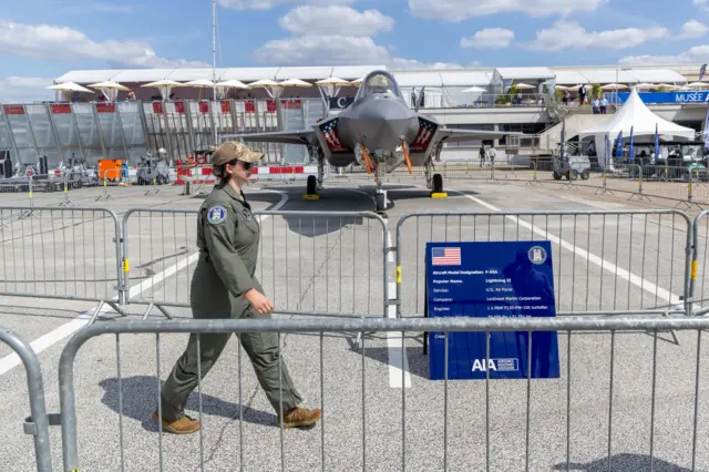 Uma pessoa vestida com traje de piloto caminha em frente a um F-35 A Lightning II de nova geração, fabricado nos Estados Unidos, exposto durante o primeiro dia da 55ª edição do Salão Internacional de Aeronáutica de Paris, no Aeroporto de Paris-Le Bourget, próximo a Paris, França, em 16 de junho de 2025